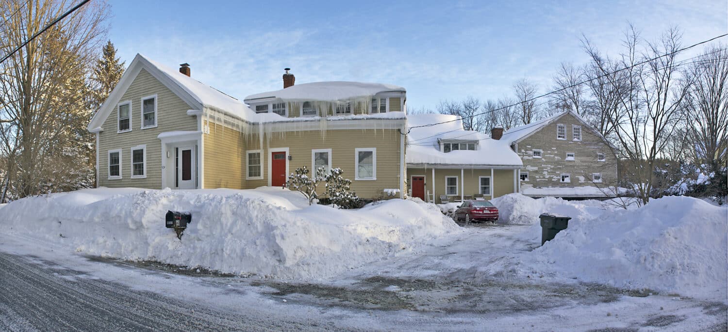 Massachusetts home showing severe ice dam formation and icicles along roof edge requiring immediate professional roof repair.