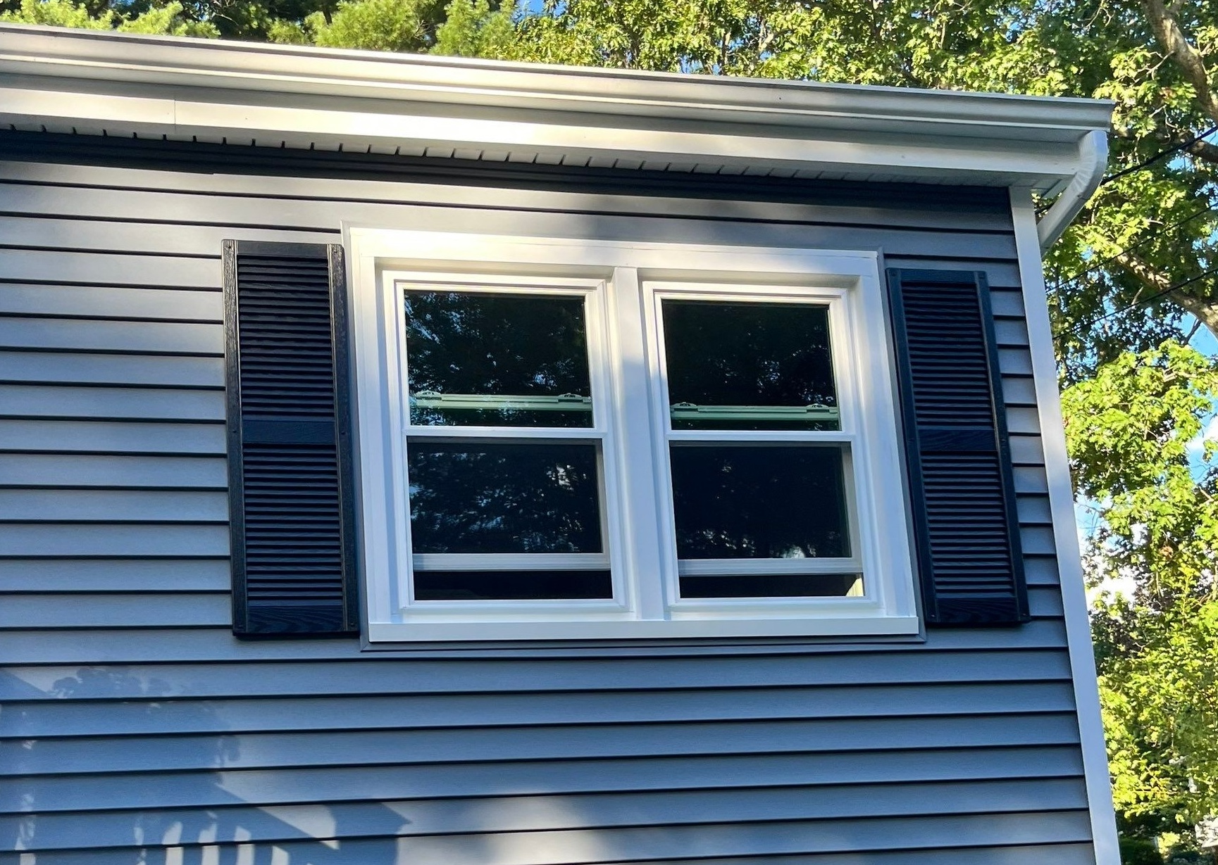White replacement double-hung windows installed on gray vinyl siding home to improve energy efficiency in summer.