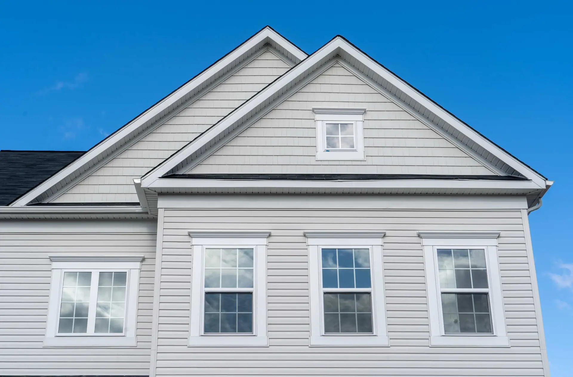 Front view of a modern, light gray house with white trim, featuring multiple windows designed for window safety and a gabled roof, set against a clear blue sky.