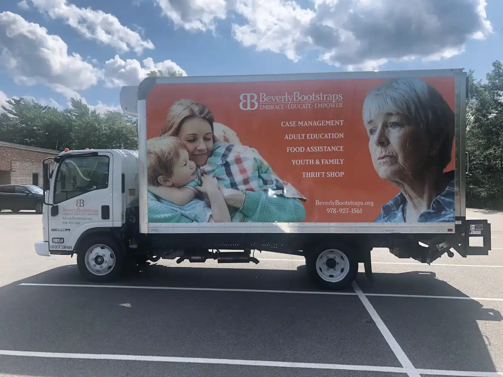 A white box truck with a Beverly Bootstraps ad shows a smiling woman with a child and a concerned older woman, promoting case management, education, food assistance, youth programs, and a thrift shop in covid-19 Massachusetts.