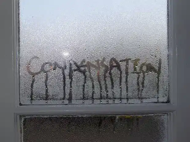 Condensation on windows covers a window pane, with the word CONDENSATION written through the moisture, letting light shine through the letters.