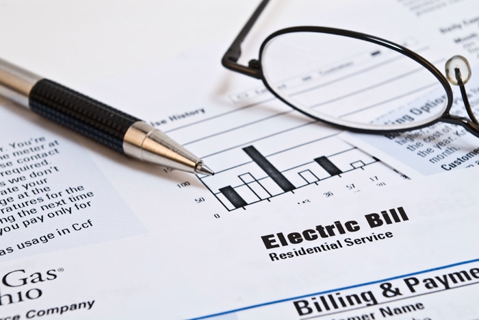 Close-up of an electric bill with a bar graph, a pen, and eyeglasses resting on top—highlighting tips to save money on your monthly expenses. The documents are labeled Electric Bill and Billing & Payment.