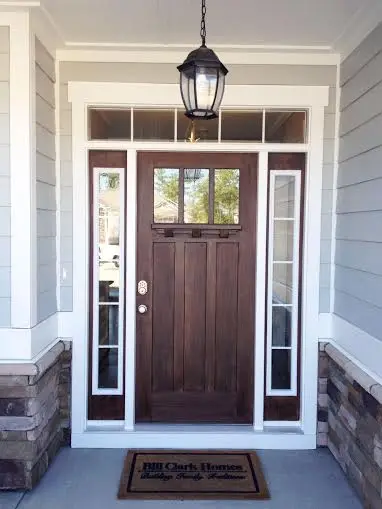 A wooden front door with glass panels on both sides and above, with a hanging lantern overhead. A doormat that reads Bill Clark Homes sits in front—perfect inspiration if you’re ready to use your tax refund for your next home improvement project.