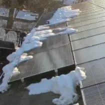 Solar panels on a roof in winter, with patches of snow partially covering some panels while others remain clear.