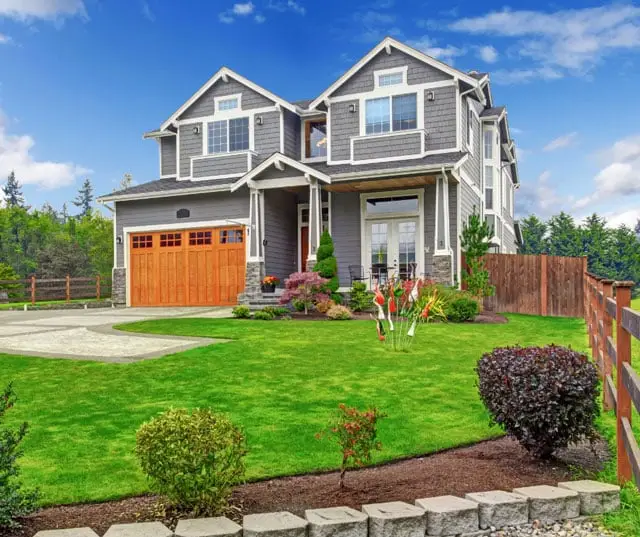 Two-story gray house with white trim and a wooden garage door, surrounded by a well-manicured green lawn. Enjoy the siding benefits of durability and curb appeal—perfect for your spring siding replacement projects.